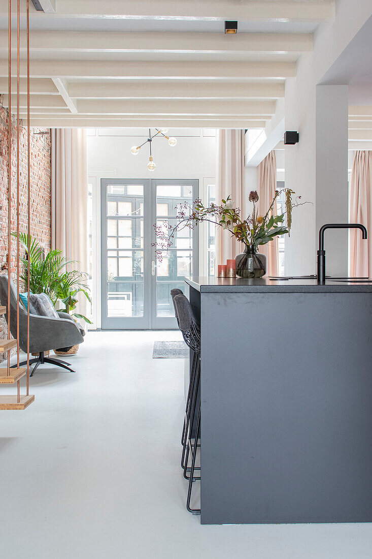 Modern open-plan kitchen with black cooking island, bar stools and view of living room with glass doors