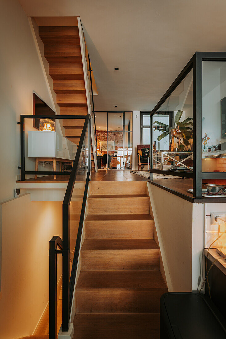 Staircase with wooden steps and black banister leads to modern living room