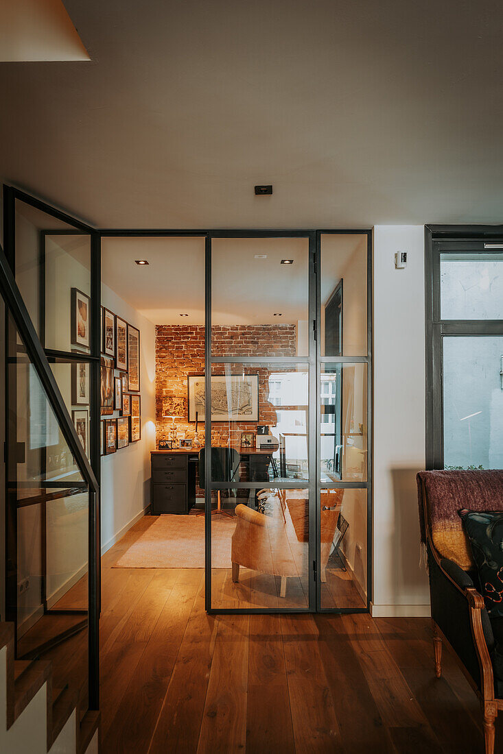 View through glass door in modern loft style into home office in front of brick wall