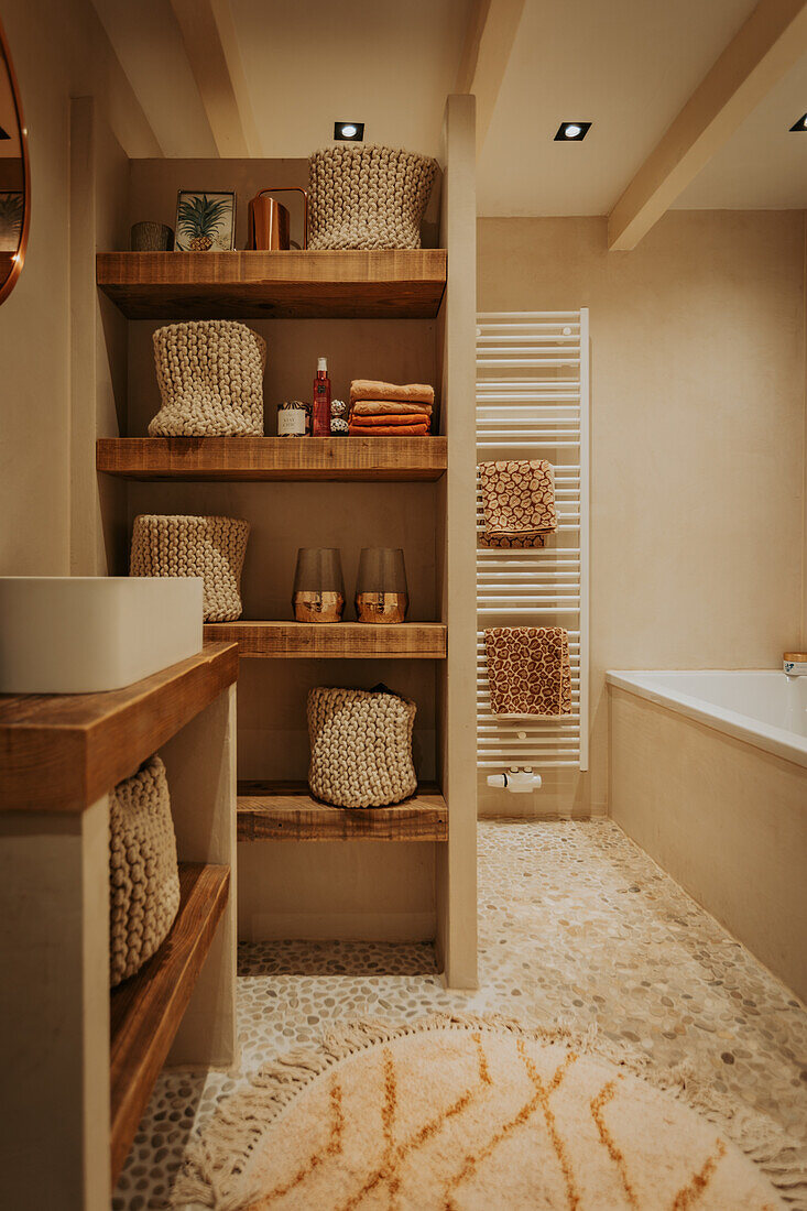 Bathroom with wooden shelves and knitted baskets with stone floor and bathtub