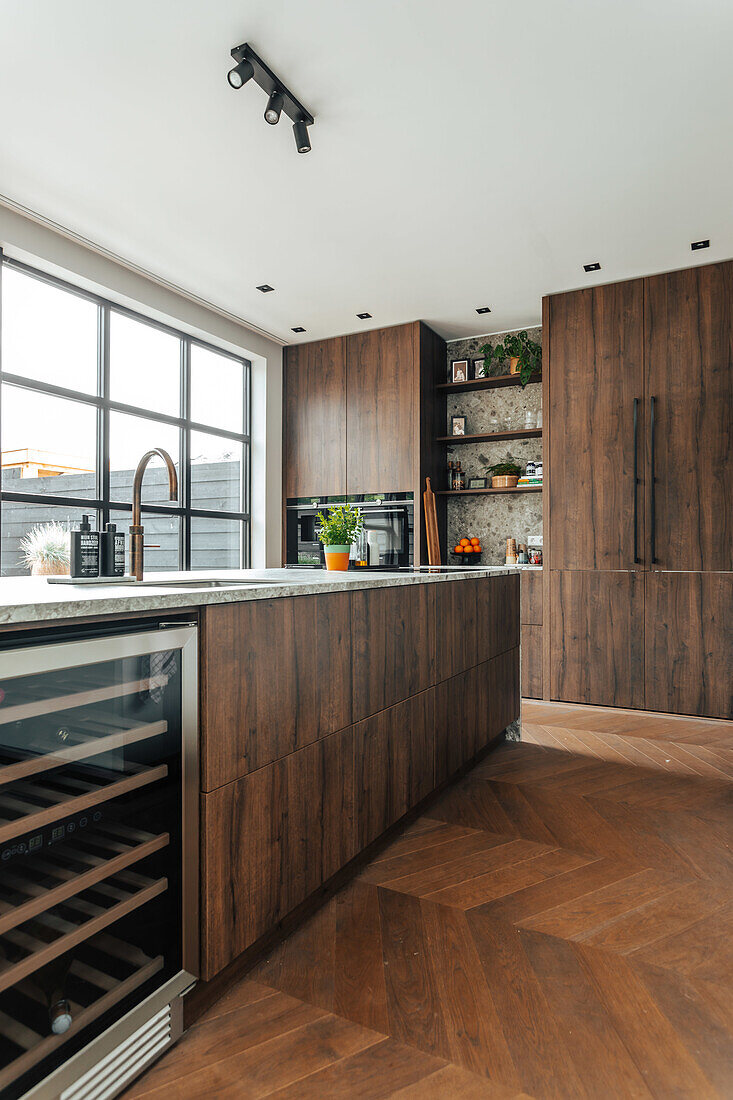 Modern kitchen with dark wooden cupboards, large window and herringbone parquet flooring