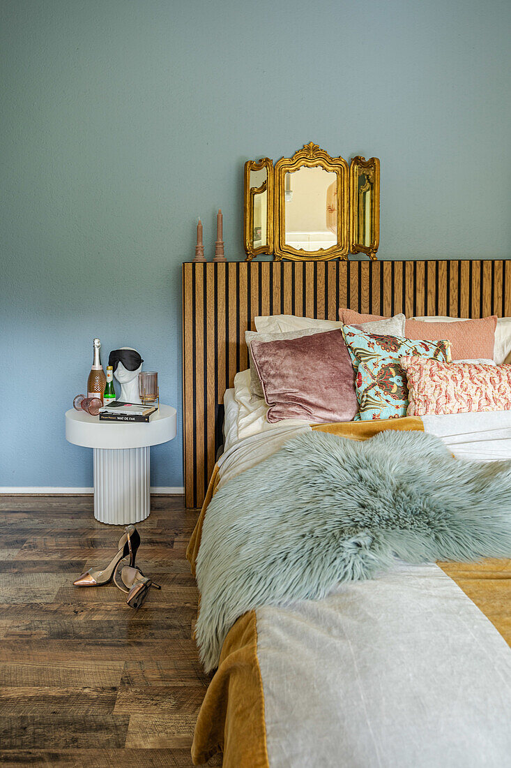 Bedroom with wooden paneled headboard, fluffy blanket and decorative pillows in front of a blue wall