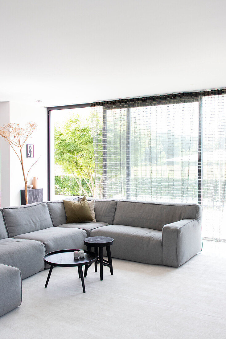 Spacious, bright living room with grey corner sofa and floor-to-ceiling windows