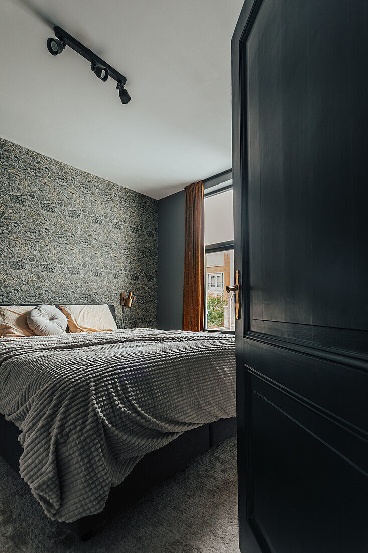 View through dark door into bedroom with patterned wallpaper wall