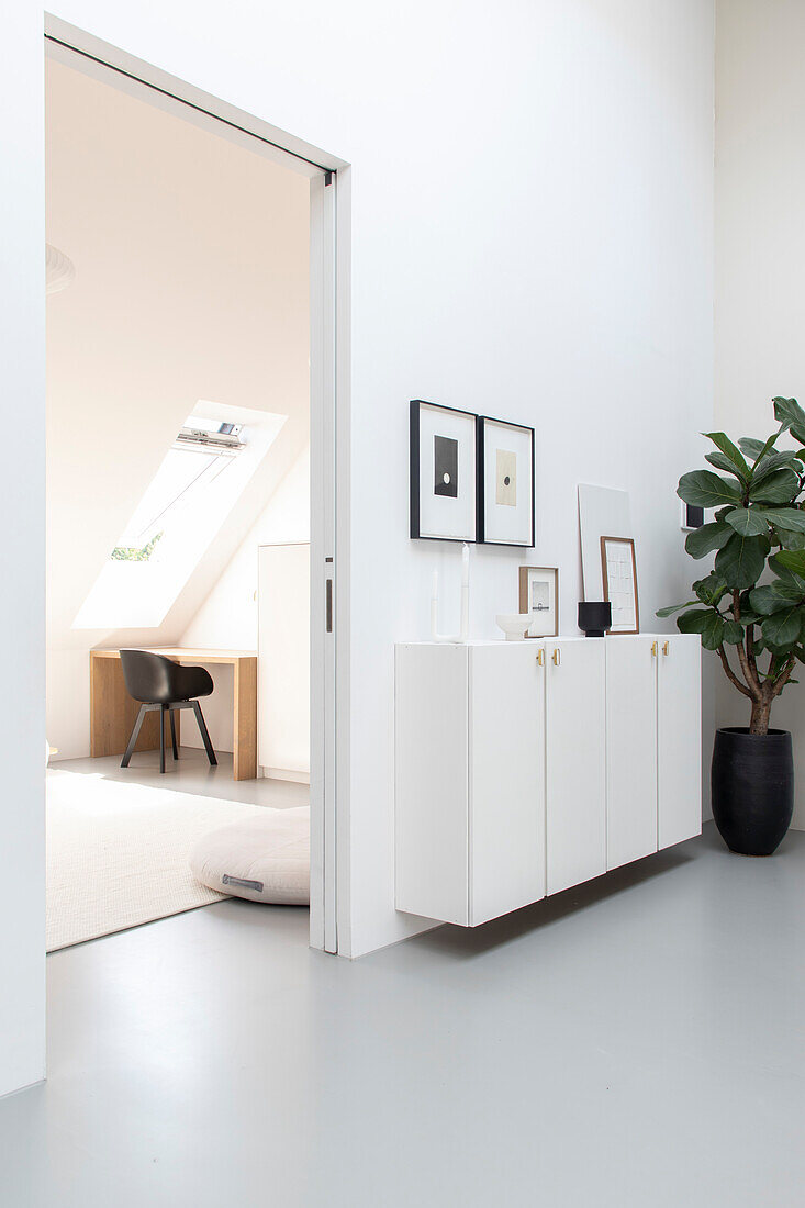 White hallway with sideboard, adjoining study with desk and skylight