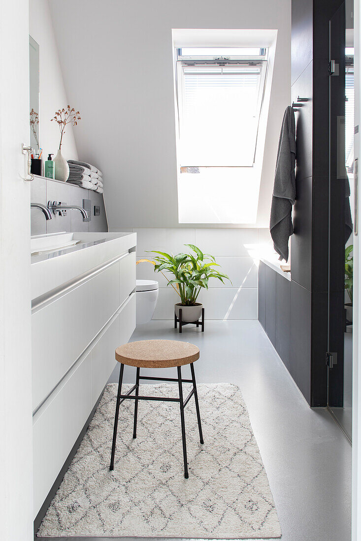 Modern bathroom with skylight, white washbasin and stool on a patterned carpet