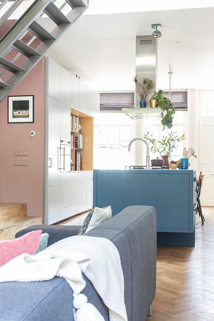 Open-plan living room with blue kitchen island and grey sofa under metal staircase