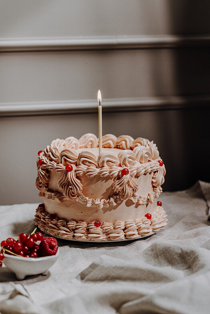 Buttercremetorte im Vintage-Stil mit Creme-Rüschen, Johannisbeeren und Kerze