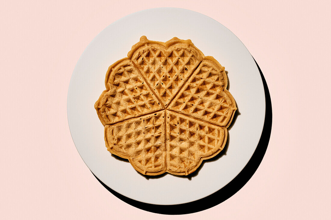 Still life scalloped heart-shape waffles on plate on pink background\n
