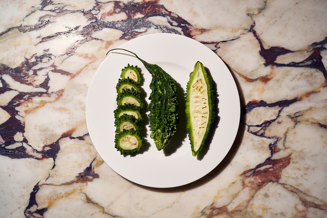 Still life green bitter melon slices and halves on plate\n