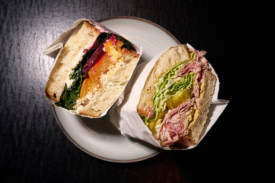 Still life gourmet sandwich halves wrapped in paper on plate\n