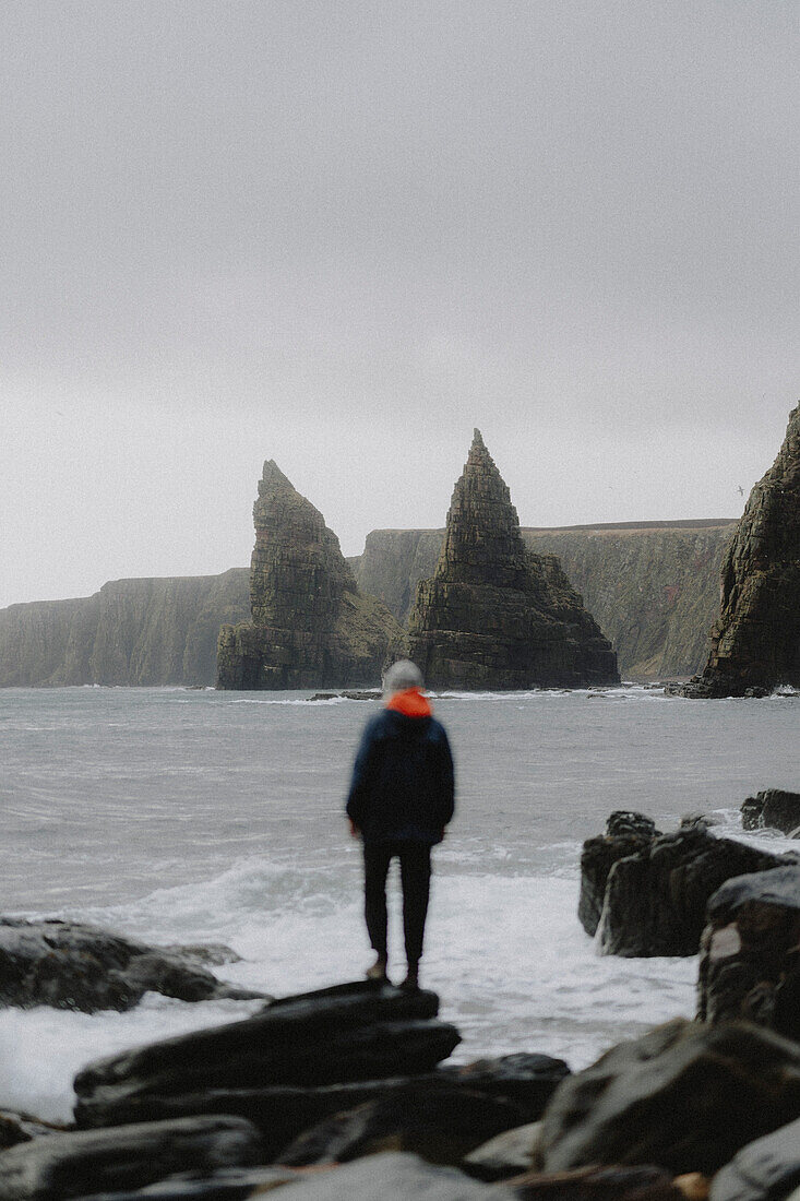 Man looking at rock formations and cliffs along ocean coastline, Duncansby, Scotland\n