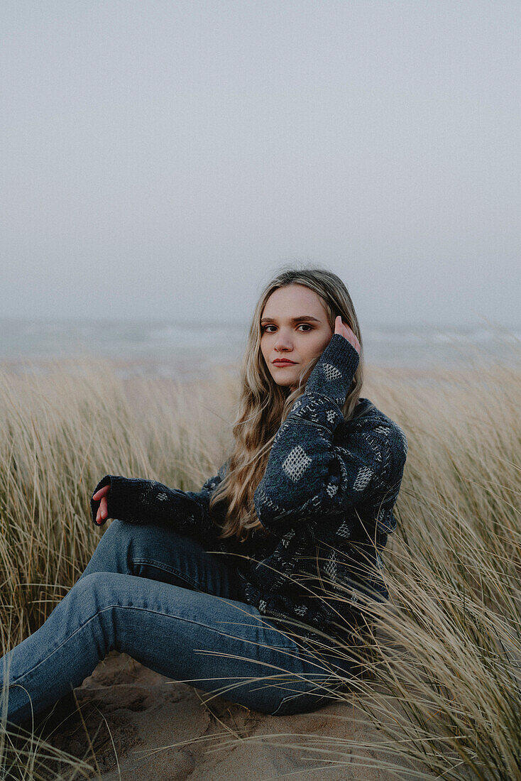 Portrait schöne junge Frau sitzt im Strandgras, Rattray, Aberdeenshire, Schottland