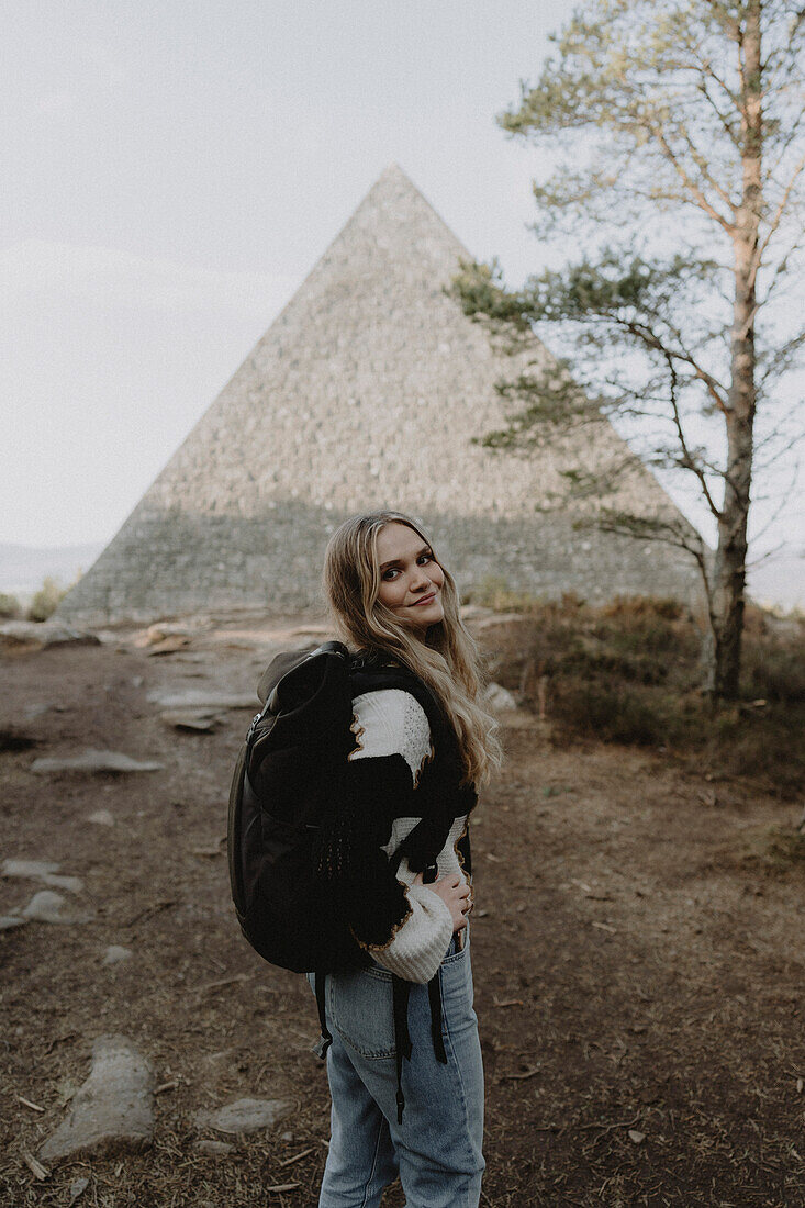 Portrait happy female hiker at stone pyramid, Balmoral, Cairngorms, Scotland\n