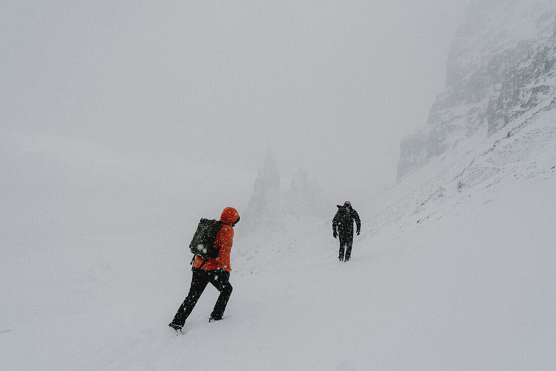 Wanderer wandern den schneebedeckten Berghang hinauf, Old Man of Storr, Isle of Skye, Schottland