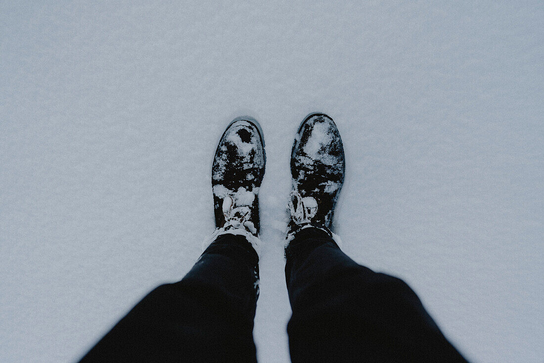 POV Blick von oben auf die Beine des Wanderers und die verschneiten Wanderschuhe