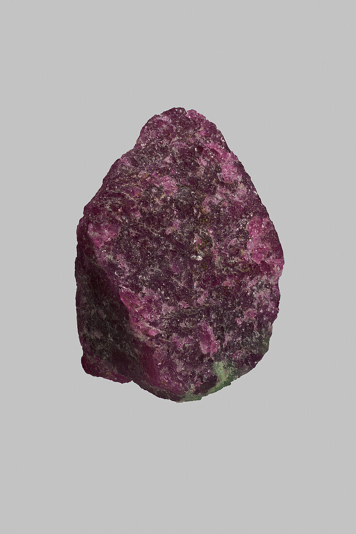 Close up textured purple Tanzanian ruby and zoisite stone on gray background\n