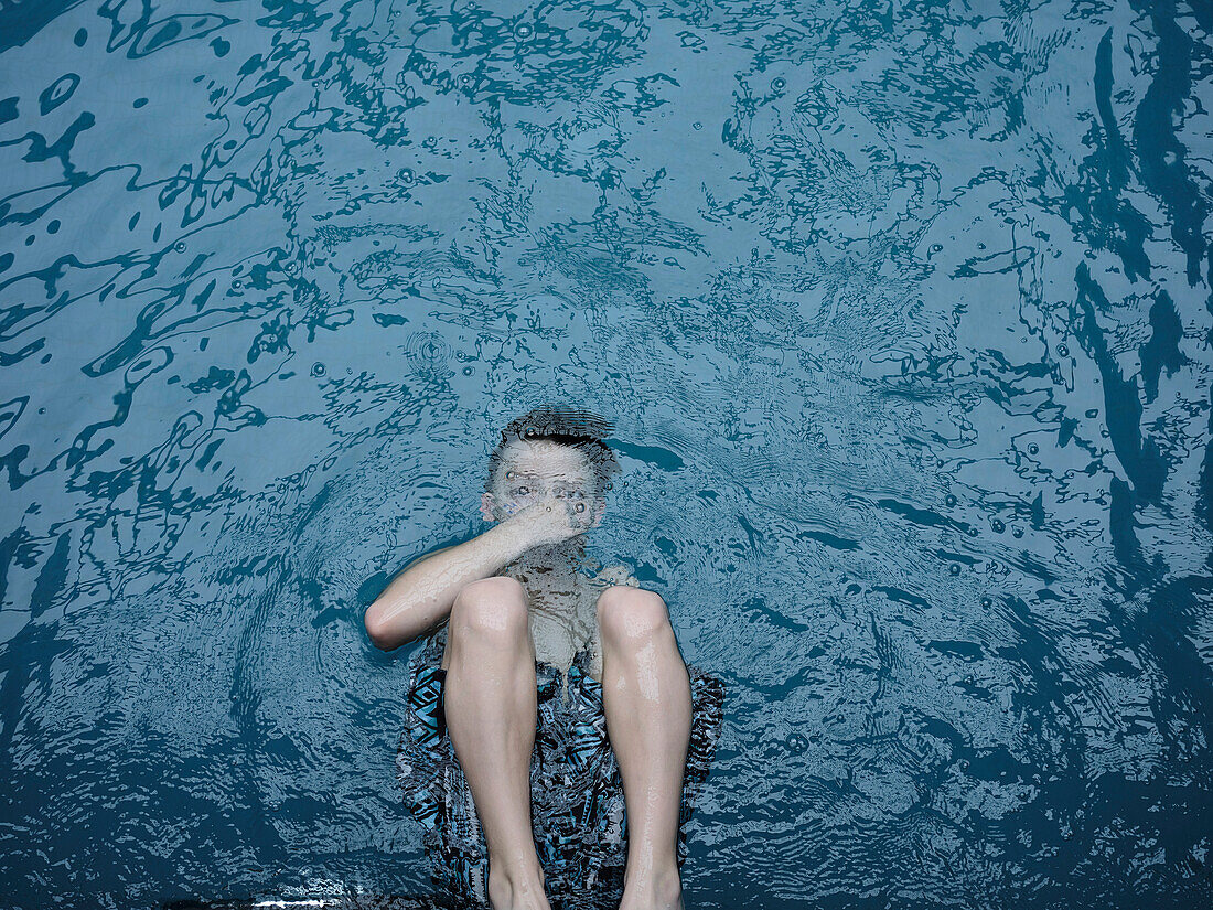 Blick von oben auf einen schwimmenden Jungen, der unter der Wasseroberfläche den Atem anhält