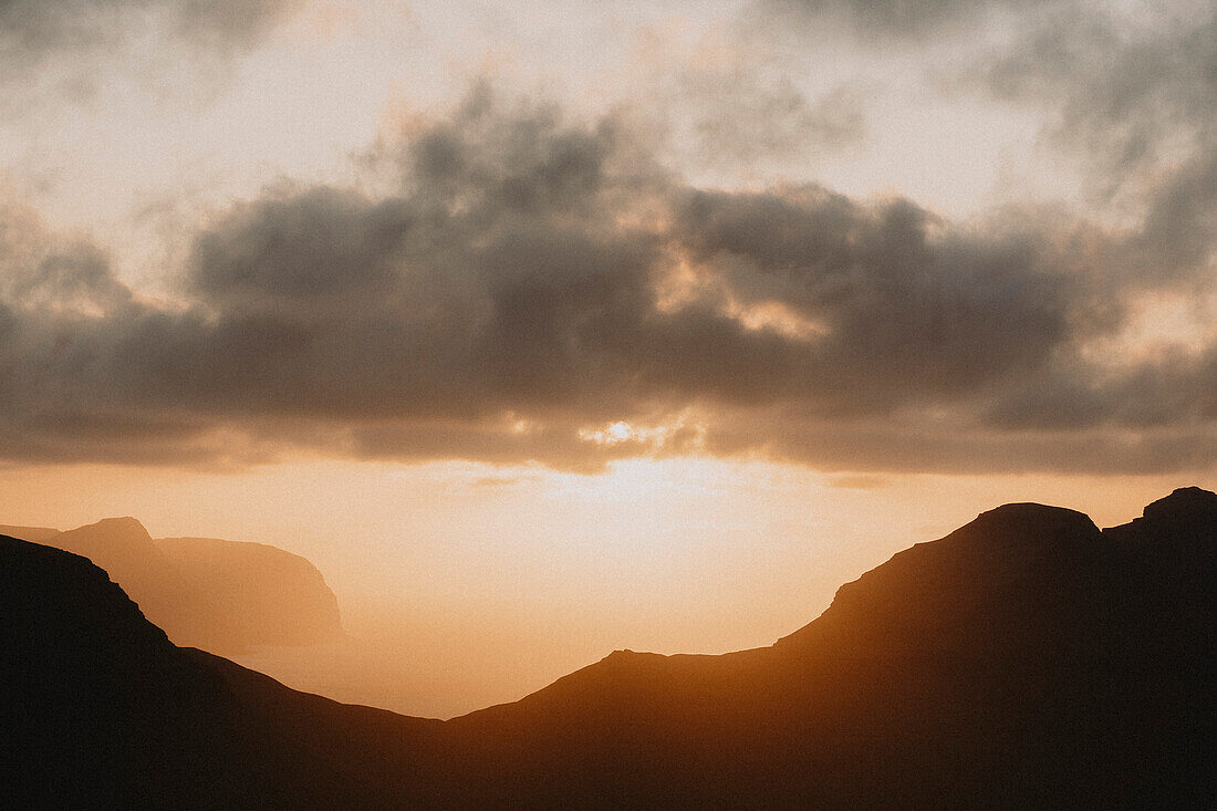 Sunset in clouds over silhouetted cliffs and sea, Klakkur, Klaksvik, Faroe Islands\n