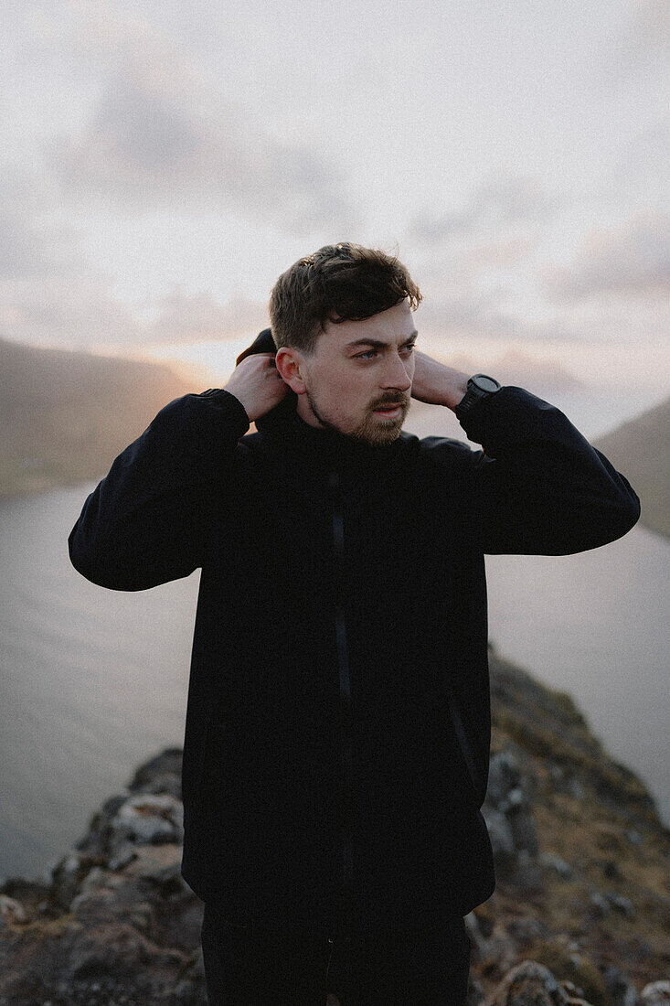 Man with hooded jacket on hill above river, Klakkur, Klaksvik, Faroe Islands\n