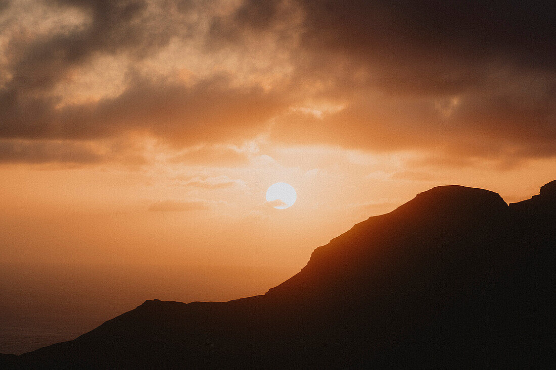 Sonnenuntergang in orangefarbenem Himmel über silhouettierten Klippen und Meer, Klakkur, Klaksvik, Färöer Inseln