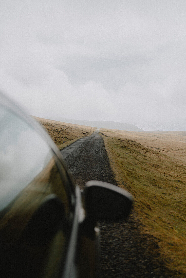 Car driving on road in remote landscape, Lopra, Suduroy, Faroe Islands\n