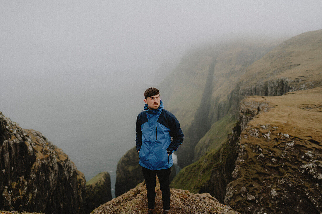 Männlicher Wanderer in Jacke auf Klippen über dem Meer, Dunnesdrangar, Vagar, Färöer Inseln