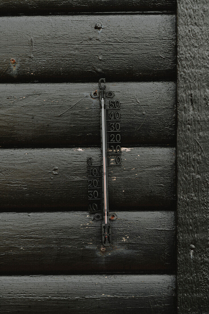 Cast iron thermometer on black wall of house\n