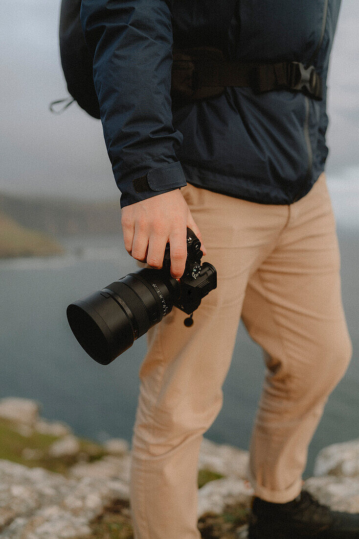 Close up hiker holding SLR camera on cliff, Neist Point, Isle of Skye, Scotland\n
