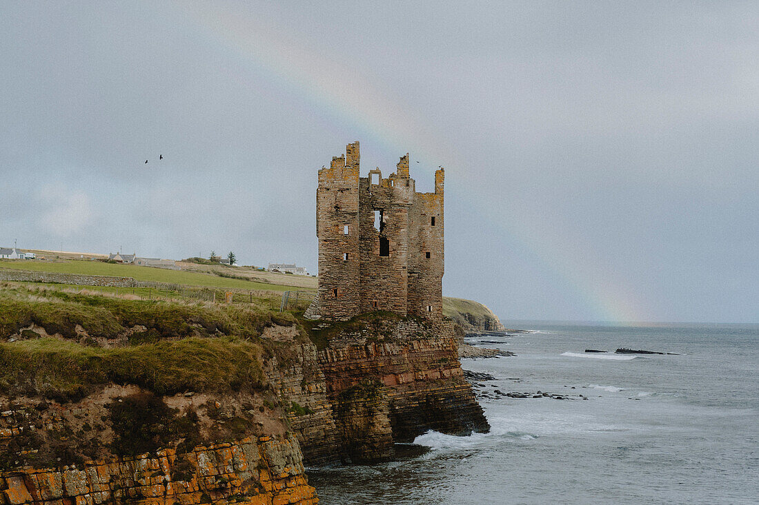 Rainbow behind castle ruins on cliff above ocean, Keiss, Scottish Highlands, Scotland\n