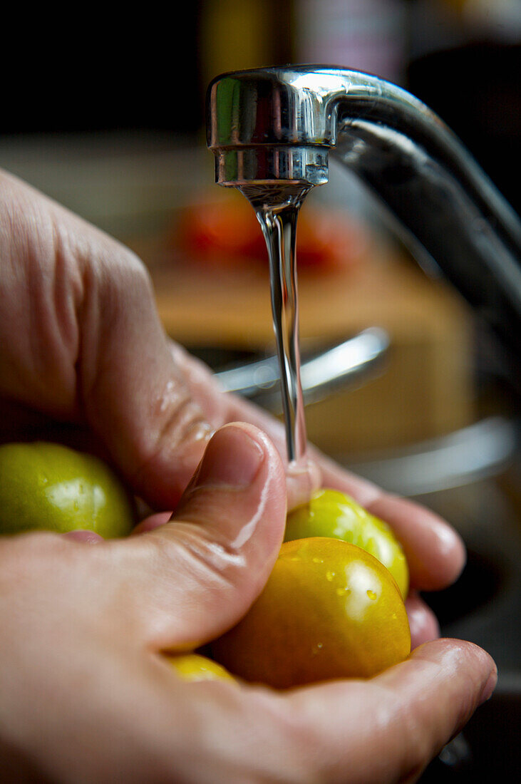 Männerhände waschen Kirschtomaten unter fließendem Wasser