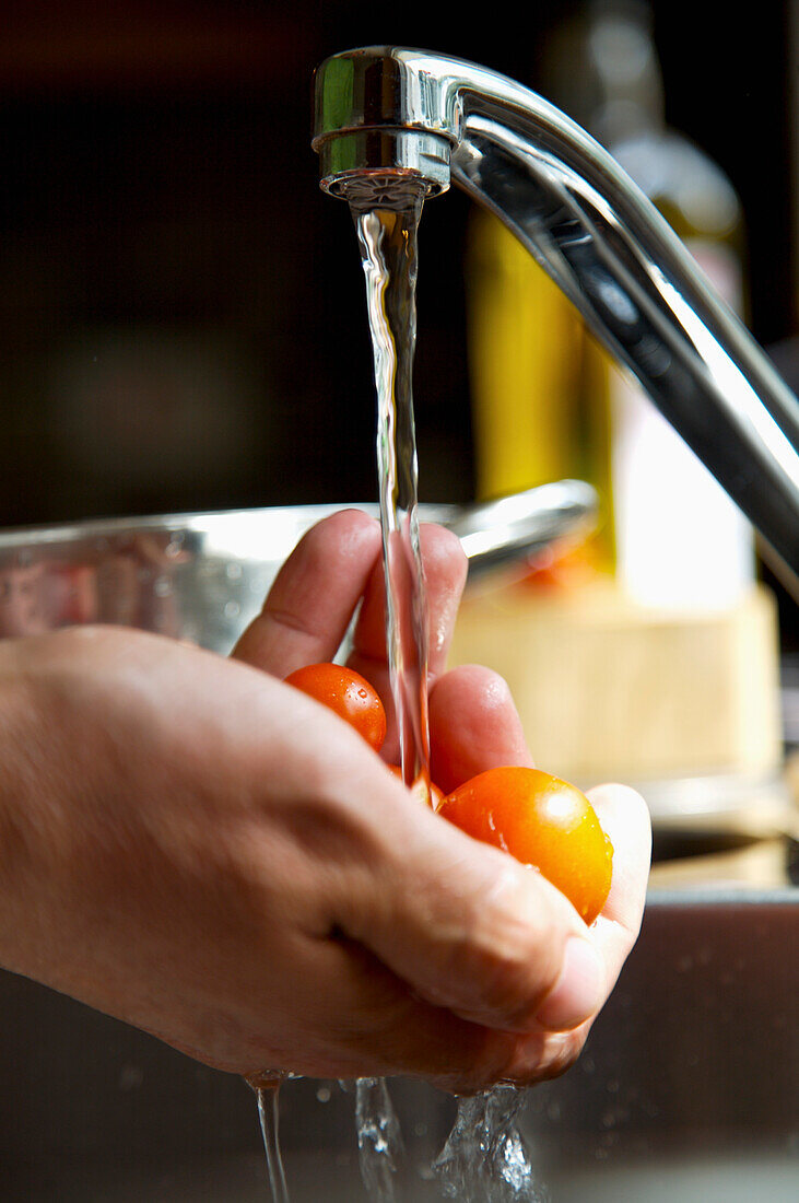 Man's hands washing cherry tomatoes with running water\n