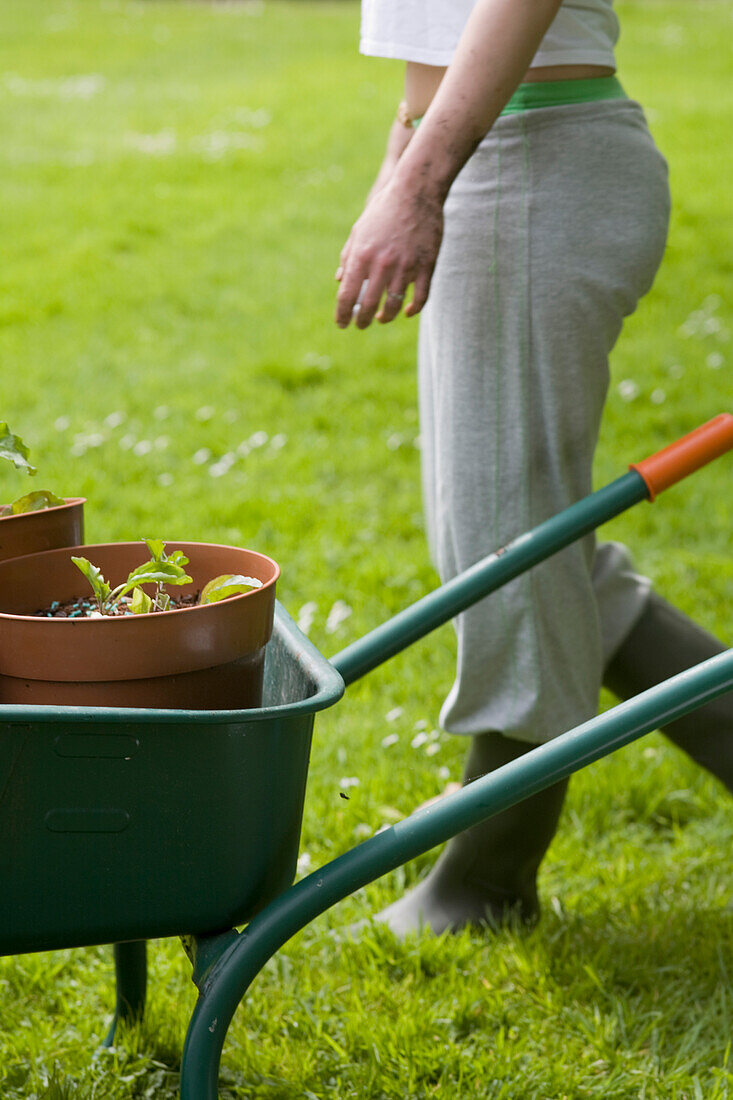 Junge Frau steht bei der Gartenarbeit neben einer Schubkarre