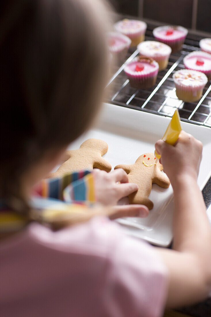 Back view of young girl decorating ginger bread man\n