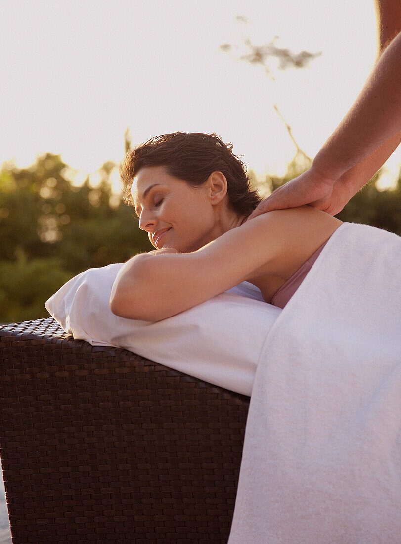 Male massage therapist massaging woman on shoulders outdoors\n