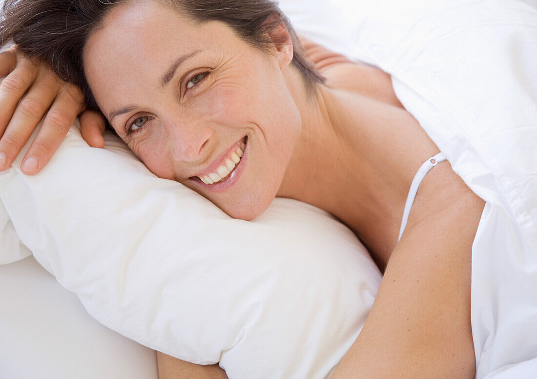 Lächelnde Frau im Bett liegend und das Kissen umarmend