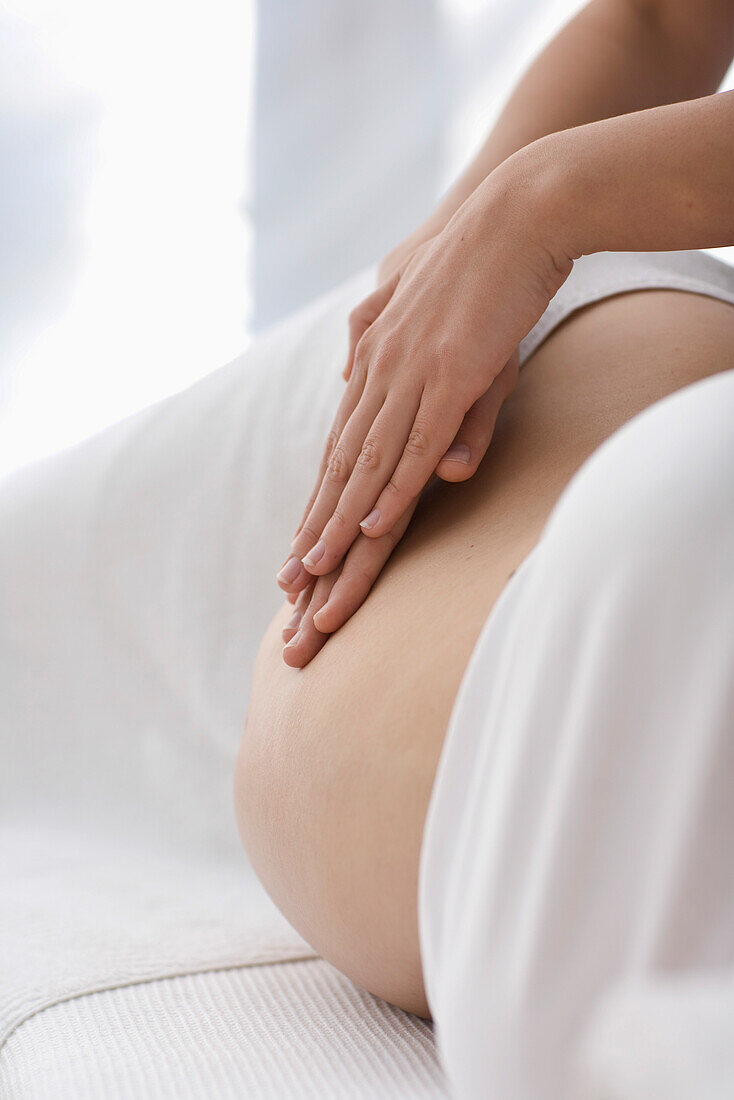 Close up of female massage therapist's hands massaging pregnant woman stomach\n