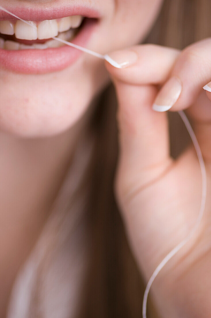 Close up of young woman flossing front teeth\n