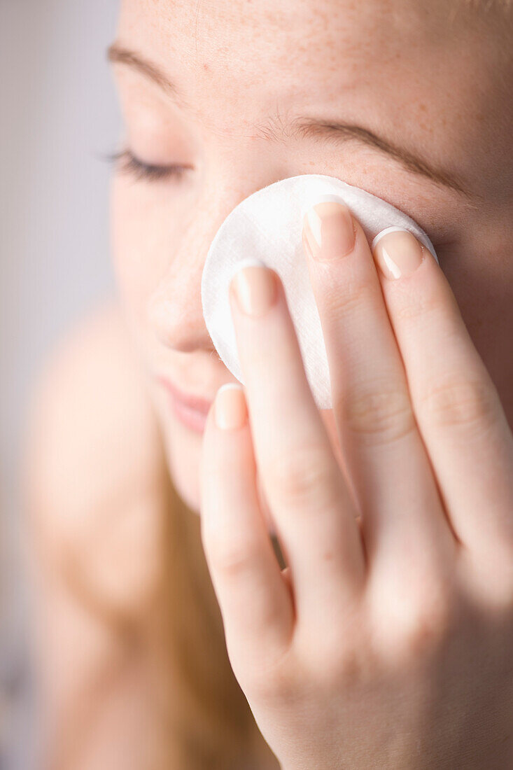 Close up of young woman removing make up with white cotton pad\n