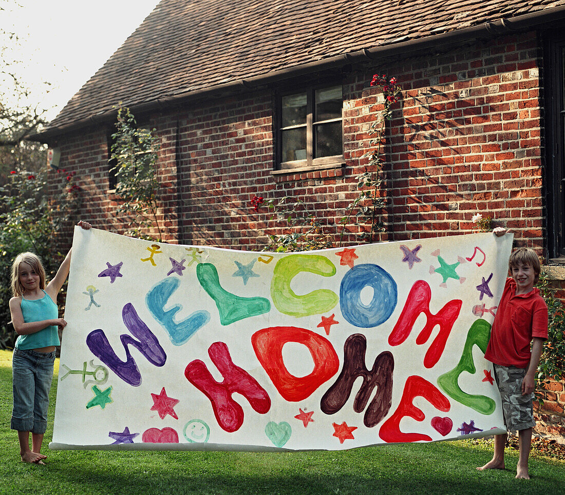 Portrait of two young children holding colorful welcome home sign\n