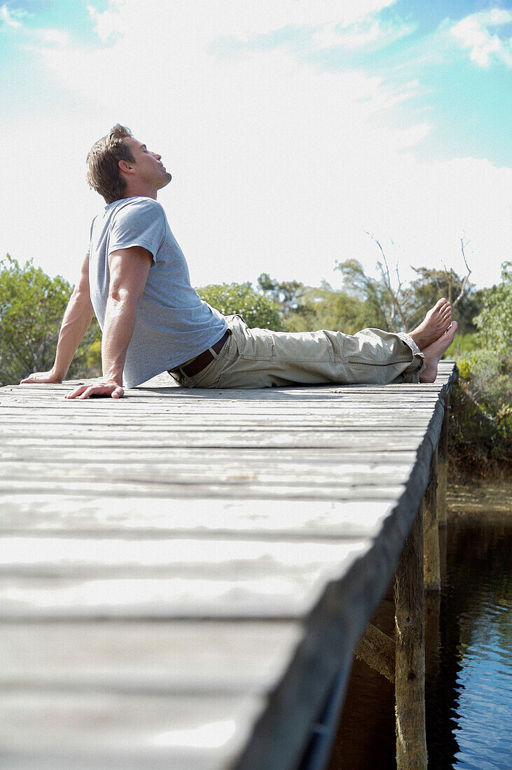 Portrait of barefoot man sitting on a boardwalk by a river\n