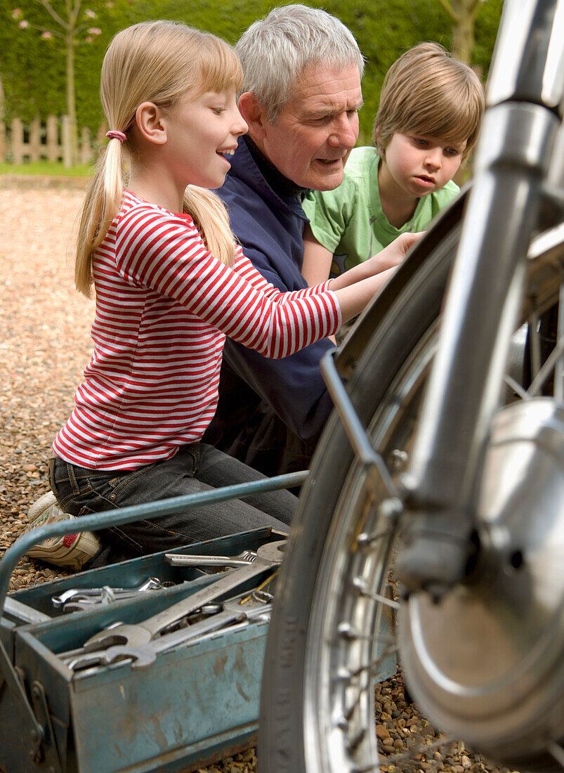 Enkelkinder helfen Großvater bei der Reparatur eines Motorrads