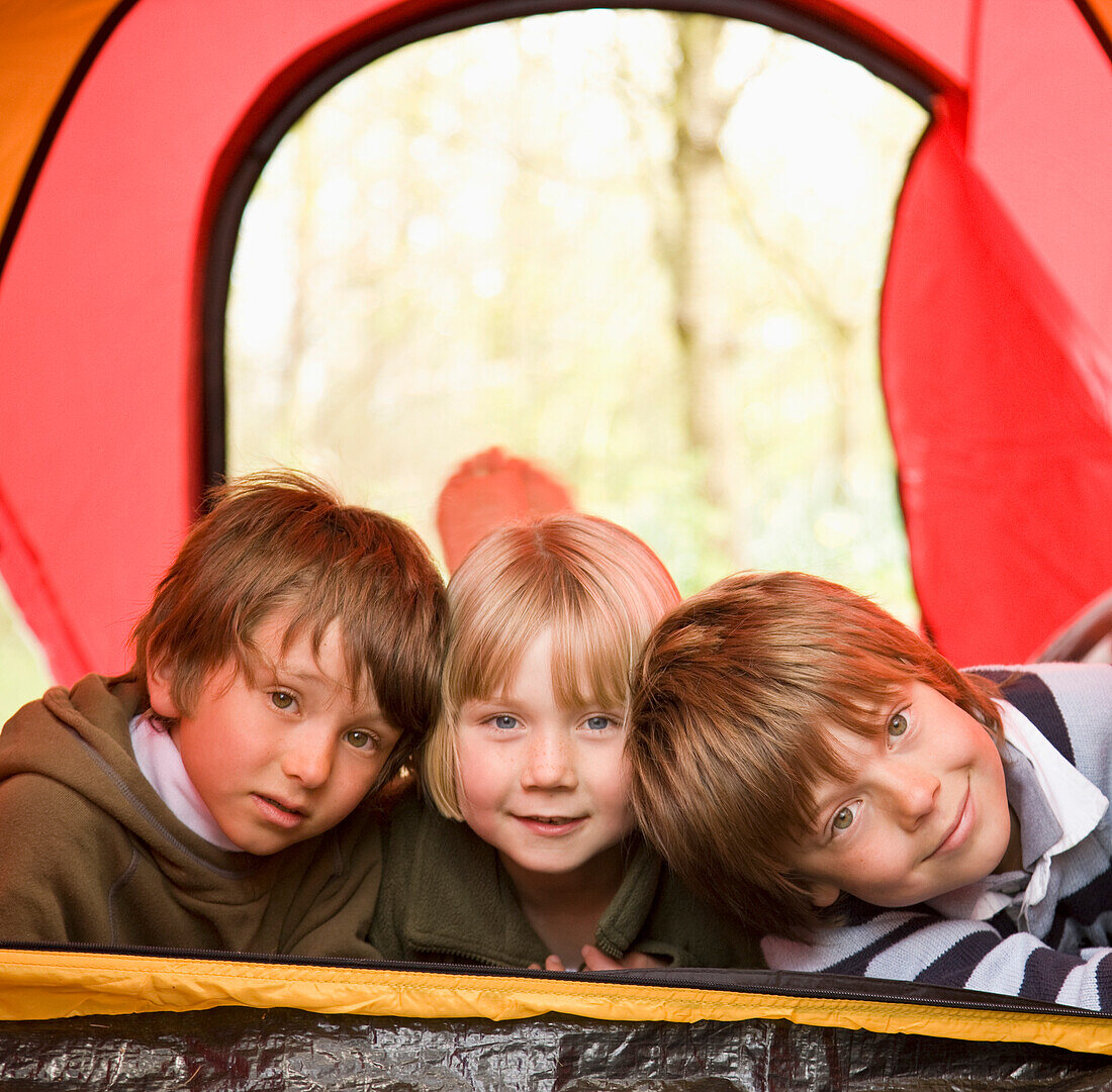 Portrait of three children lying in a tent\n