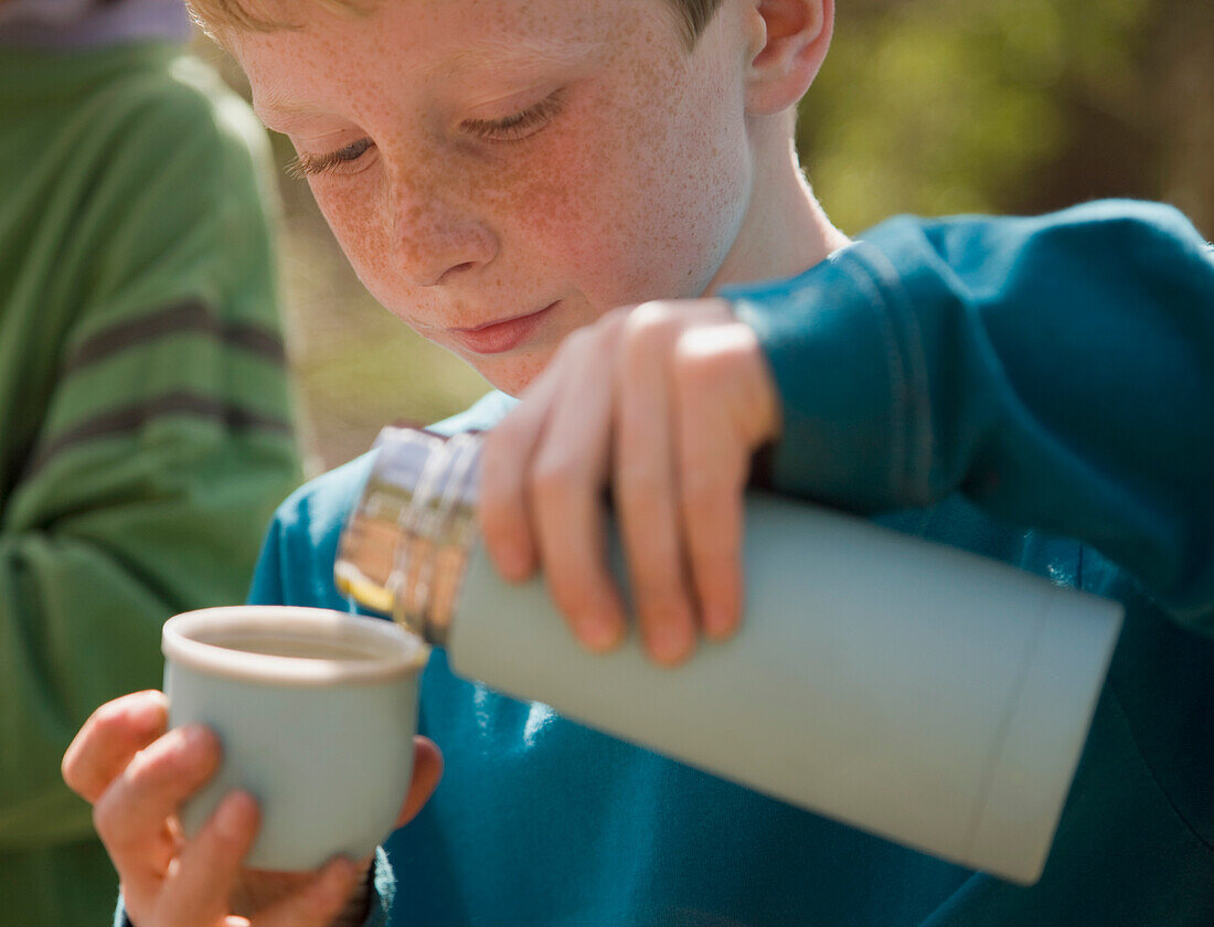 Nahaufnahme eines Jungen, der Wasser aus einer Isolierflasche gießt