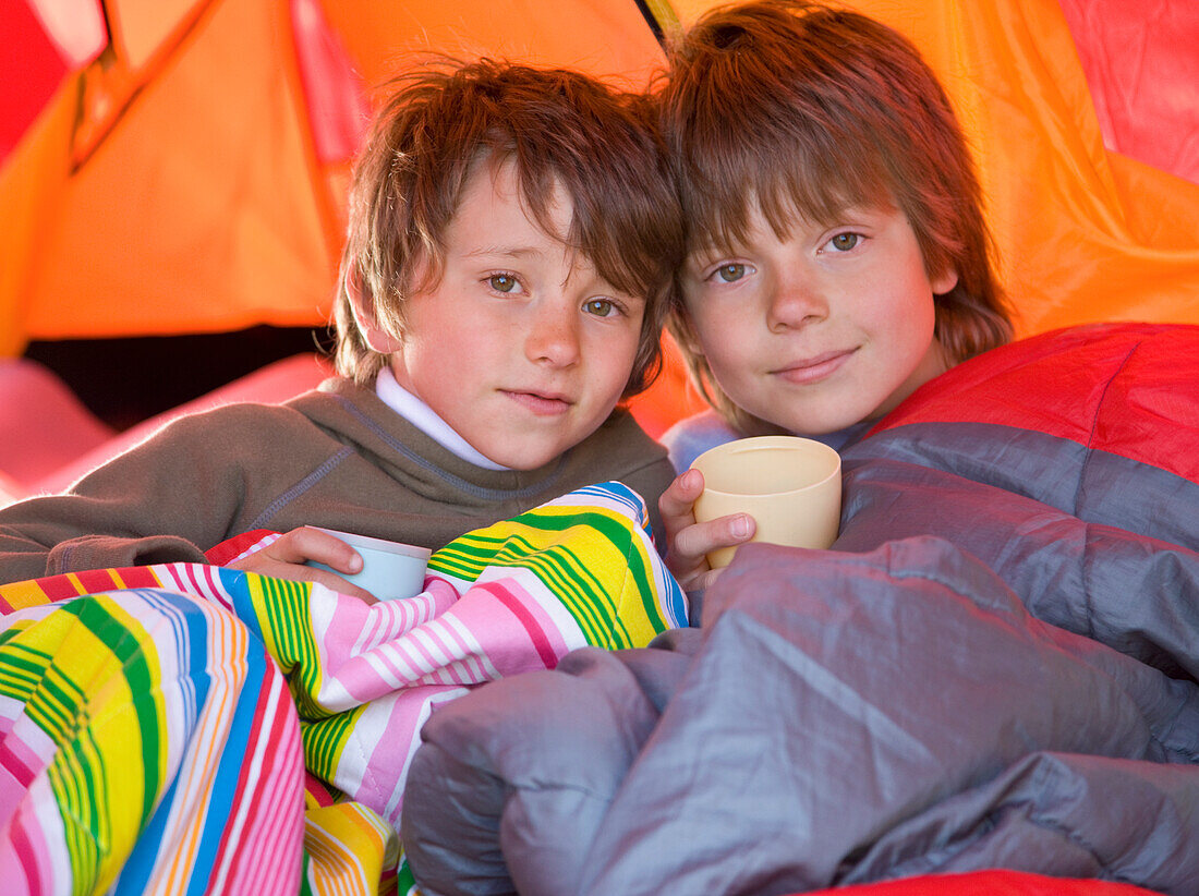 Porträt von zwei Jungen in Schlafsäcken im Zelt sitzend