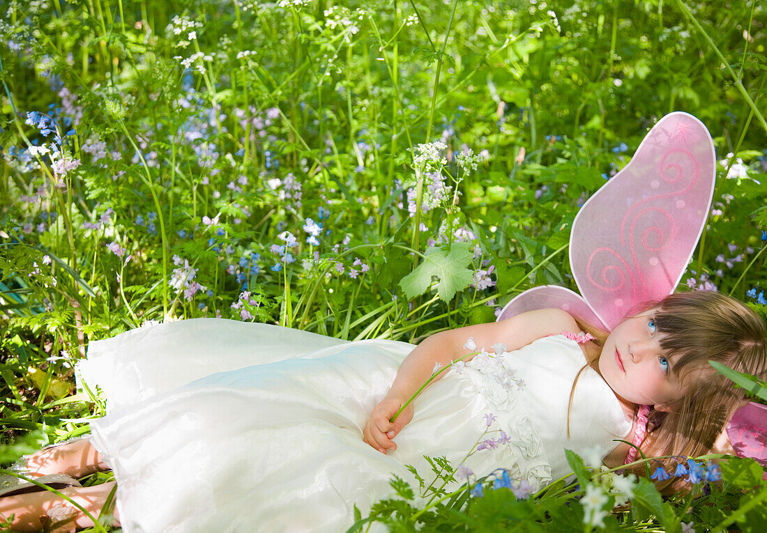 Portrait of a young girl in a fairy costume lying in a field of flowers\n