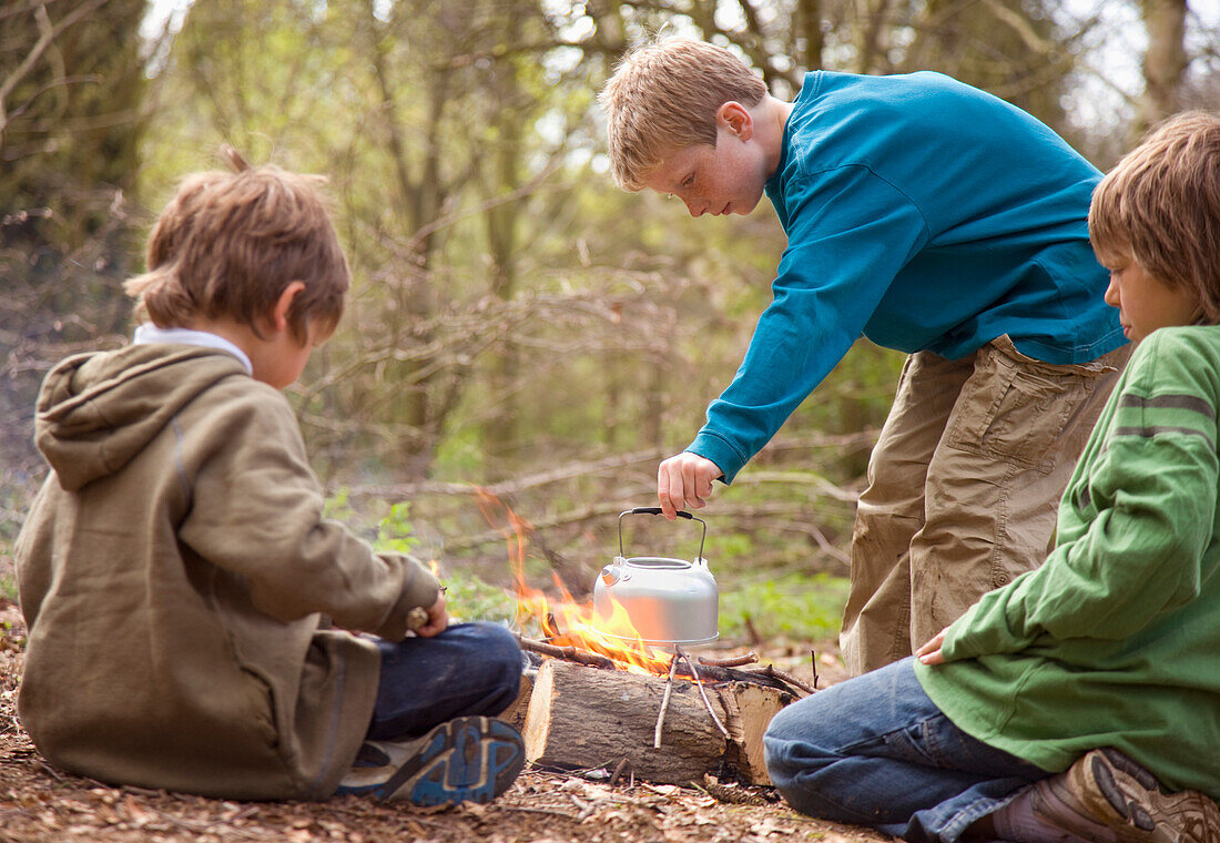 Drei Jungen am Lagerfeuer kochen Wasser in einem Kessel