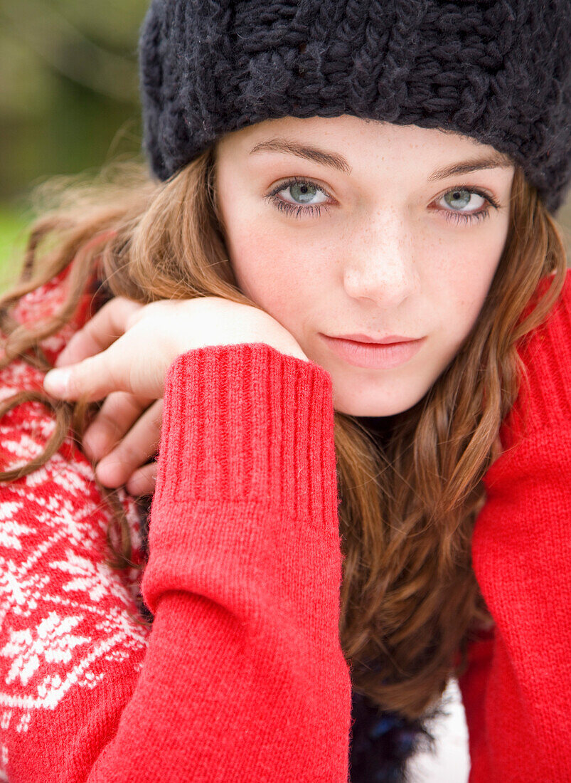 Close up of teenaged girl wearing woolly hat with face resting on hands\n