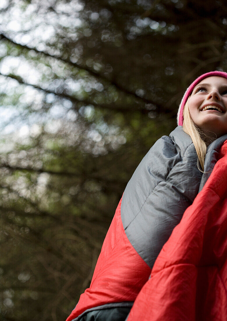 Standing teenaged girl wrapped in a sleeping bag looking up and smiling\n