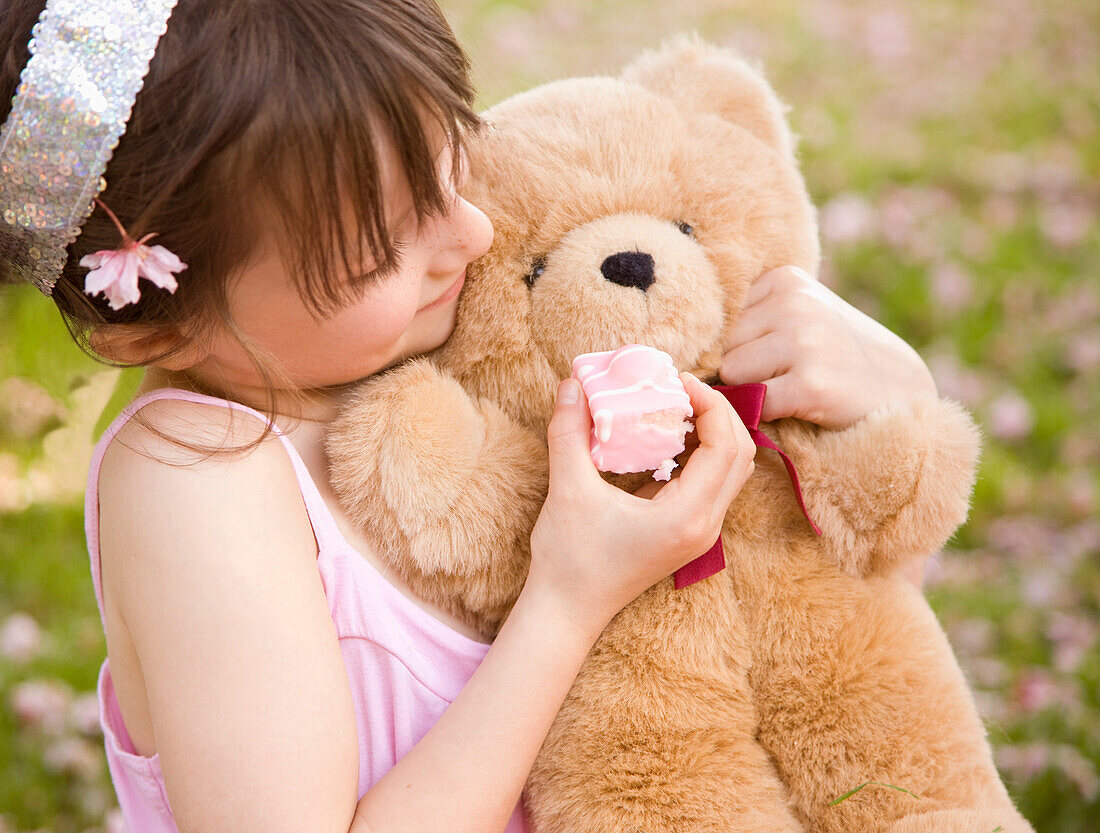 Young girl holding and feeding cake to a teddy bear\n